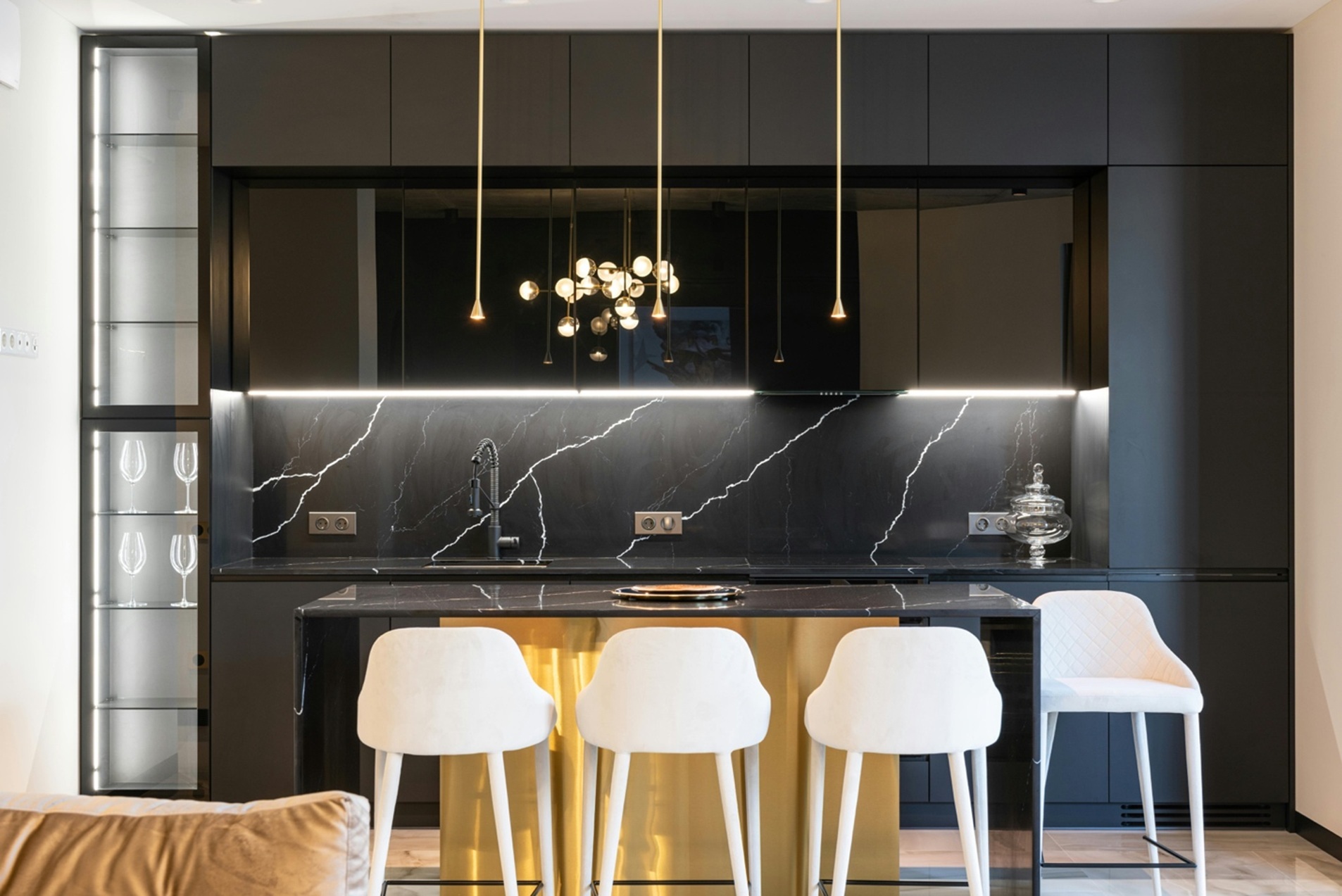 a gold and black marbled kitchen with an island and white chairs